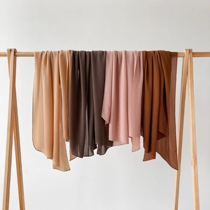 Detail view of pleated chiffon hijabs in earth tones hanging on wooden hangers
