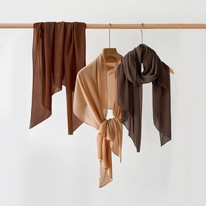 Detail of pleated silk-like scarves in caramel and apricot hanging on wooden racks
