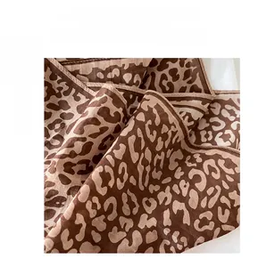 Detailed close-up of leopard print silk scarf fabric texture and rolled edge stitching