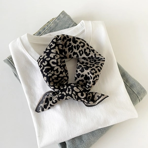 Detailed view of silk leopard print scarf knot styled with white shirt and blue jeans