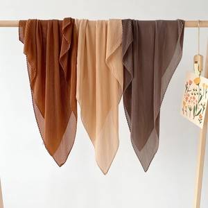 Detailed view of three pleated chiffon hijabs in earth tones hung on a wooden rack