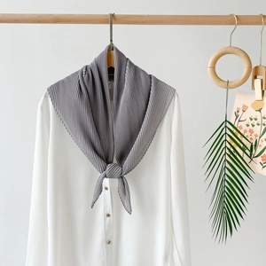 Detail view of a grey pleated chiffon scarf styled on a white shirt with aesthetic props