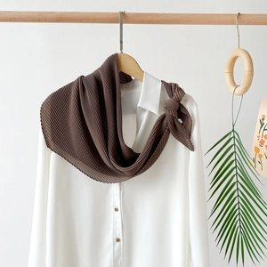 Detail of dark brown pleated chiffon scarf hanging on a minimalist wooden hanger
