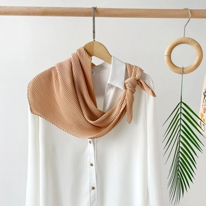 Close-up of pleated skin-tone chiffon scarf styled on a white shirt with gold buttons