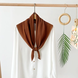 Detailed view of dark brown pleated scarf with accordion texture on white shirt garment