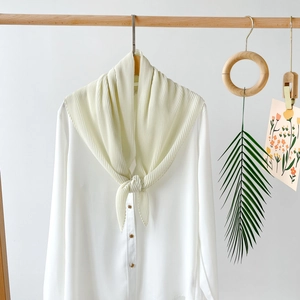 Detailed shot of beige pleated chiffon scarf paired with white long sleeve silk blouse