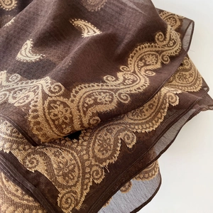 Detailed close-up of brown silk scarf showing golden paisley embroidery and sheer texture