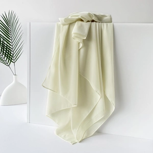 Detail eines hellbeigen Schals aus Chiffon mit glatter Textur auf weißem Podest