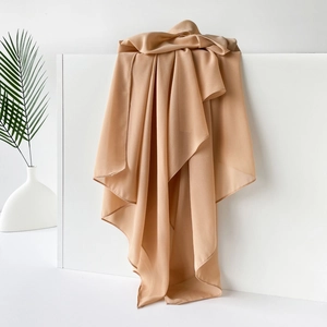 Detailansicht eines camelfarbenen Schals aus Chiffon, elegant drapiert auf weißem Podest