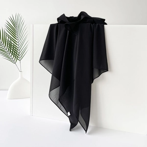 Detailansicht eines schwarzen Satin-Hijabs, elegant auf weißem Podest mit Pflanzen