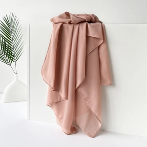 Detail eines staubrosa Chiffonschals auf weißen Blöcken mit grünem Palmenblatt-Akzent