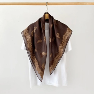 Detailed texture of brown silk scarf with golden paisley patterns on a white tee
