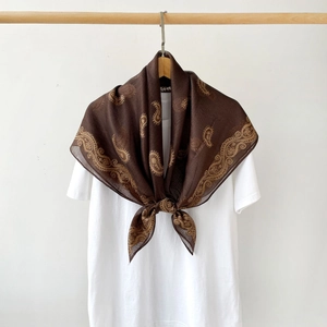Close-up of a brown and gold paisley silk scarf styled on a white shirt and wooden hanger