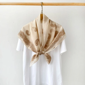 Detailed view of champagne paisley silk scarf tied on a white t-shirt for a chic look