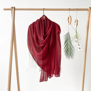 Detailansicht eines weinroten Satin-Hijab-Schals an einem Holzbügel mit Naturdeko