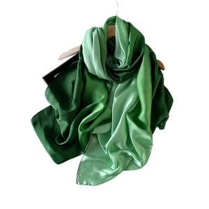 Elegant gradient green satin silk scarf draped over a wooden hanger near a black gift box