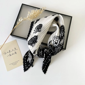 Detailed shot of pleated silk scarf with black and white rose print on artistic tray
