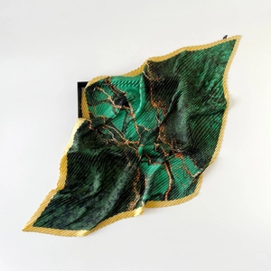Detail of dark green pleated silk scarf with golden abstract patterns and wavy edges