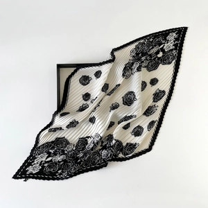 Detail of pleated silk scarf with black and white rose print on a minimalist tray
