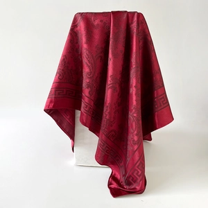 Détail d'un foulard en soie rouge foncé à motifs paisley sur une plateforme blanche