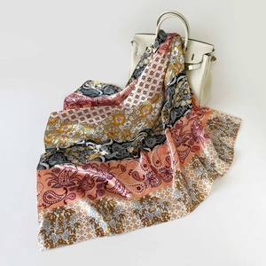 Dettaglio di un foulard di seta con stampa paisley drappeggiato su una borsa in pelle
