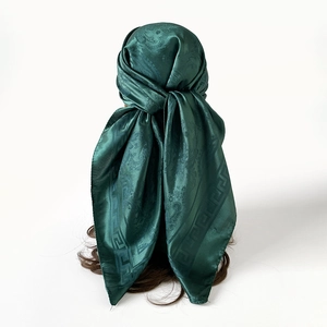 Détail d'un foulard en satin vert foncé à motif paisley, porté comme accessoire de tête élégant