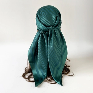 Elegant dark green satin square silk scarf with geometric pattern on wavy brown hair