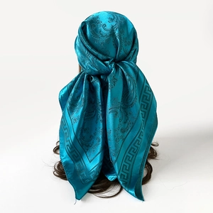 Vue détaillée d'un foulard en satin bleu paon noué sur les cheveux avec motifs de paisley