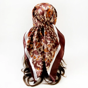 Dettaglio di un foulard quadrato in raso maculato legato su lunghi capelli castani