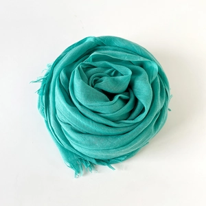 Detail of teal cotton linen scarf folded in rose shape with natural fringe edges