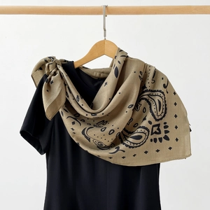 Detail of beige paisley silk square scarf with geometric patterns draped on a hanger