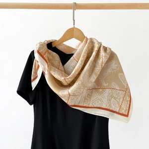 Vue détaillée d'une écharpe cachemire beige aux bordures orange sur un haut noir et cintre