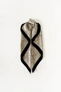 Dettaglio ravvicinato di un foulard in seta satinata con motivi paisley e bordi neri chic