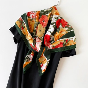 Floral print square silk scarf with vibrant orange flowers and green border on a black dress