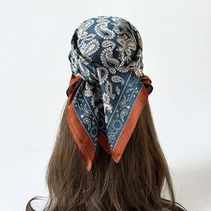 Dettaglio di un foulard di seta blu navy con motivo paisley annodato tra i capelli