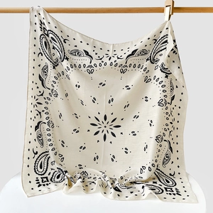 Detail view of paisley pattern square scarf hanging on a wooden bar with soft fabric drapes