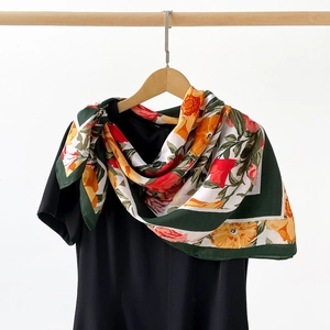 Detailed close-up of a floral silk scarf with green borders tied as a neck accessory