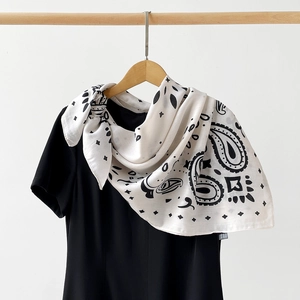 Close-up of a white silk paisley scarf with black star patterns hanging on a wood hanger