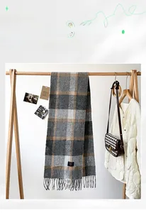 Detail of grey and beige check cashmere scarf with soft fringe on a wooden hanger