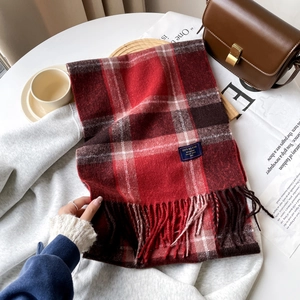 Close-up of red and black plaid scarf with fringe tassels and a 100% blend woven label