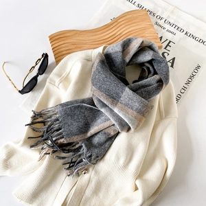 Detailed view of grey and beige plaid cashmere scarf with tassel edges and soft texture