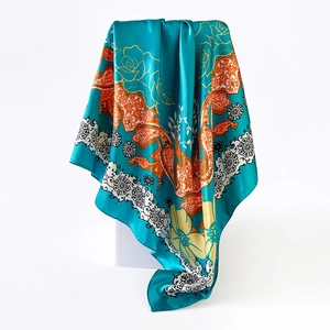 Close-up of teal silk satin square scarf featuring orange paisley floral patterns and lace details