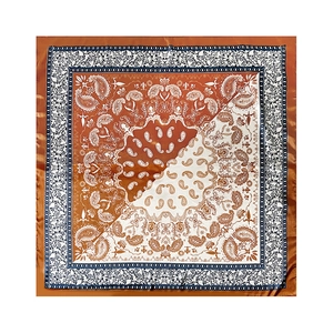 Flat lay of silk square scarf featuring orange paisley patterns and navy blue borders