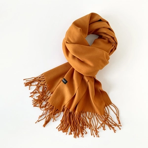 Close-up of mustard yellow scarf showing soft texture, fringe tassels, and brand label detail