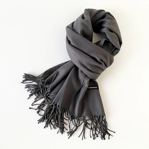 Close-up detail of dark grey cashmere scarf texture with fine fringe and brand label