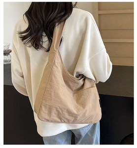 Model wearing large khaki nylon shoulder bag in a minimalist hobo style with outer pocket
