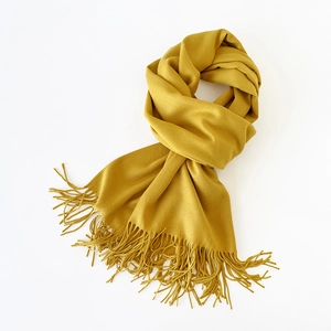Detail of soft mustard yellow scarf with fringe tassels and smooth fabric texture