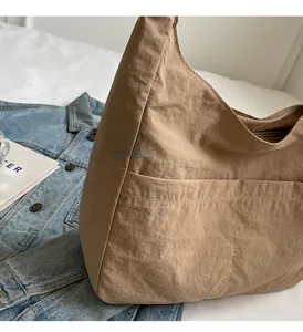 Detail of a large brown nylon hobo bag with front pockets on a white bed sheet background