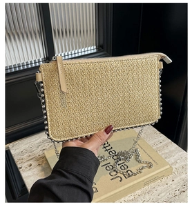 Detail of a woven straw clutch bag featuring silver beaded edges and a metal chain strap