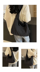 Detail view of large capacity black shoulder bag with side brand label and wide strap